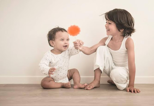 Older sibling engaging a baby with a soft toy, capturing empathy, care, and nurturing relationships nurtured at JMIS.